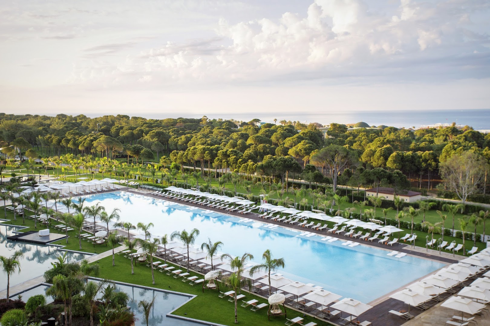 Regnum Carya galvenais baseins no putna lidojuma Belekā — plaša teritorija ar palmām, saulessargiem un priežu mežu fonā