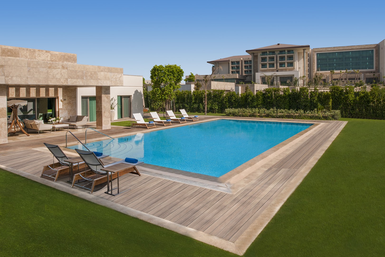 Regnum Carya plašais āra baseins pie villas ar koka klāju un ērtiem zviļņiem Belekā — skats uz viesnīcas kompleksu