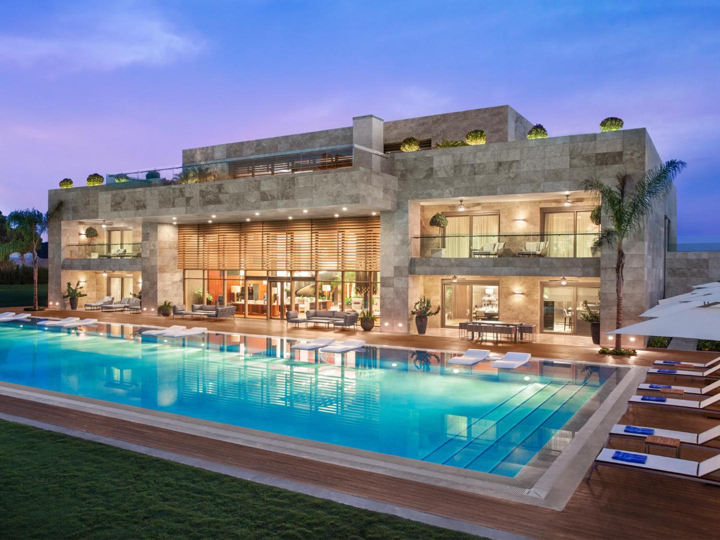Regnum Carya luksusa villa ar privātu baseinu vakarā Belekā, Turcijā — izgaismota fasāde, moderna arhitektūra un plaša atpūtas zona