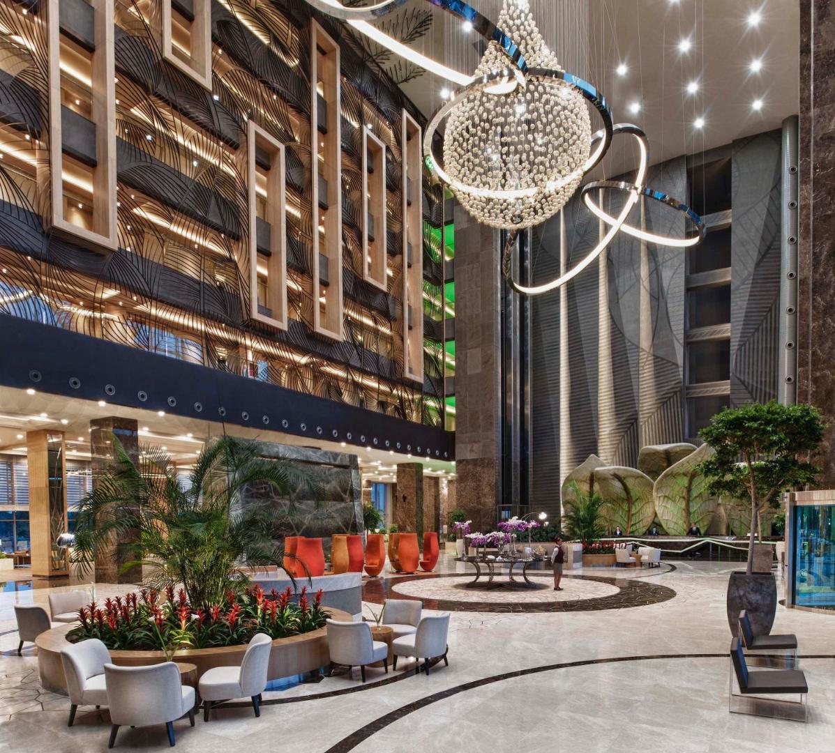 Regnum Carya iespaidīgais viesnīcas lobby ar augstiem griestiem, modernām lustrām un dizaina mēbelēm Belekā