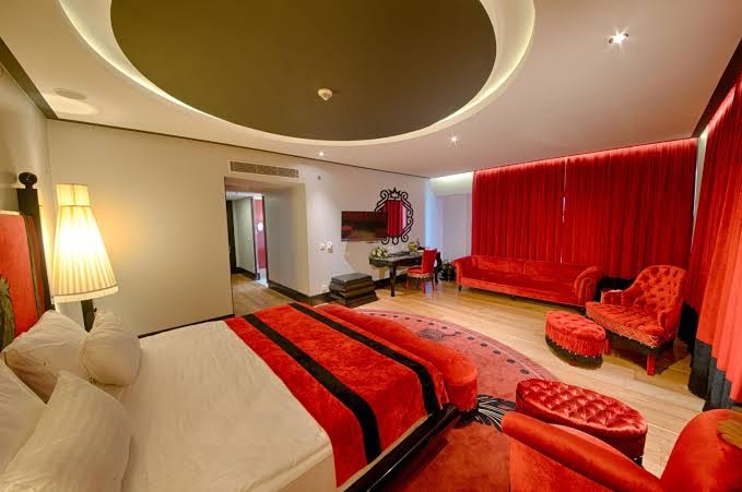 Selectum Luxury Resort luksusa numurs ar sarkanu samta dīvānu, greznu paklāju un atpūtas zonu pie loga ar sarkaniem aizkariem.