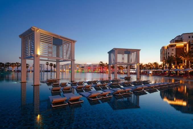 Selectum Luxury Resort āra baseins vakarā ar izgaismotām atpūtas nojumēm un sauļošanās krēsliem ūdenī Belekas reģionā, Turcijā