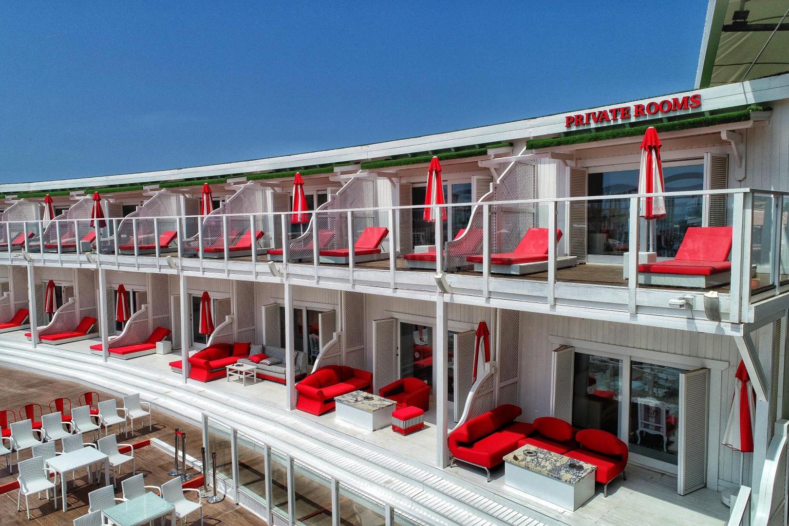 Selectum Luxury Resort divstāvu korpuss ar privātām terasēm, sarkaniem atpūtas krēsliem un saulessargiem pie baseina zonas Belekā, Turcijā.