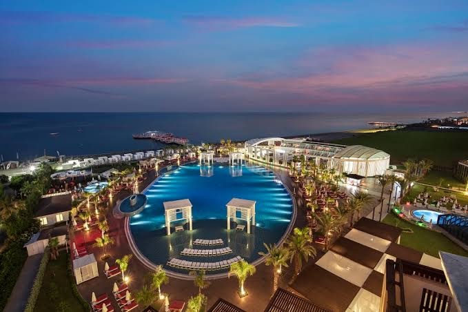 Selectum Luxury Resort panorāmas skats vakarā uz galveno baseinu, pludmali un Vidusjūru Belekā — izgaismota teritorija un palmas