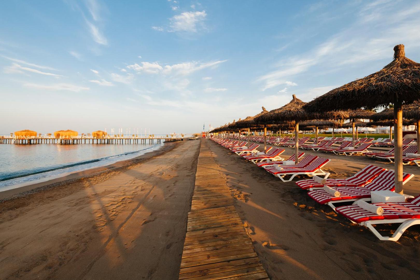 Selectum Luxury Resort privātā smilšu pludmale ar sarkani svītrainiem zviļņiem un salmu saulessargiem saulrietā Belekā