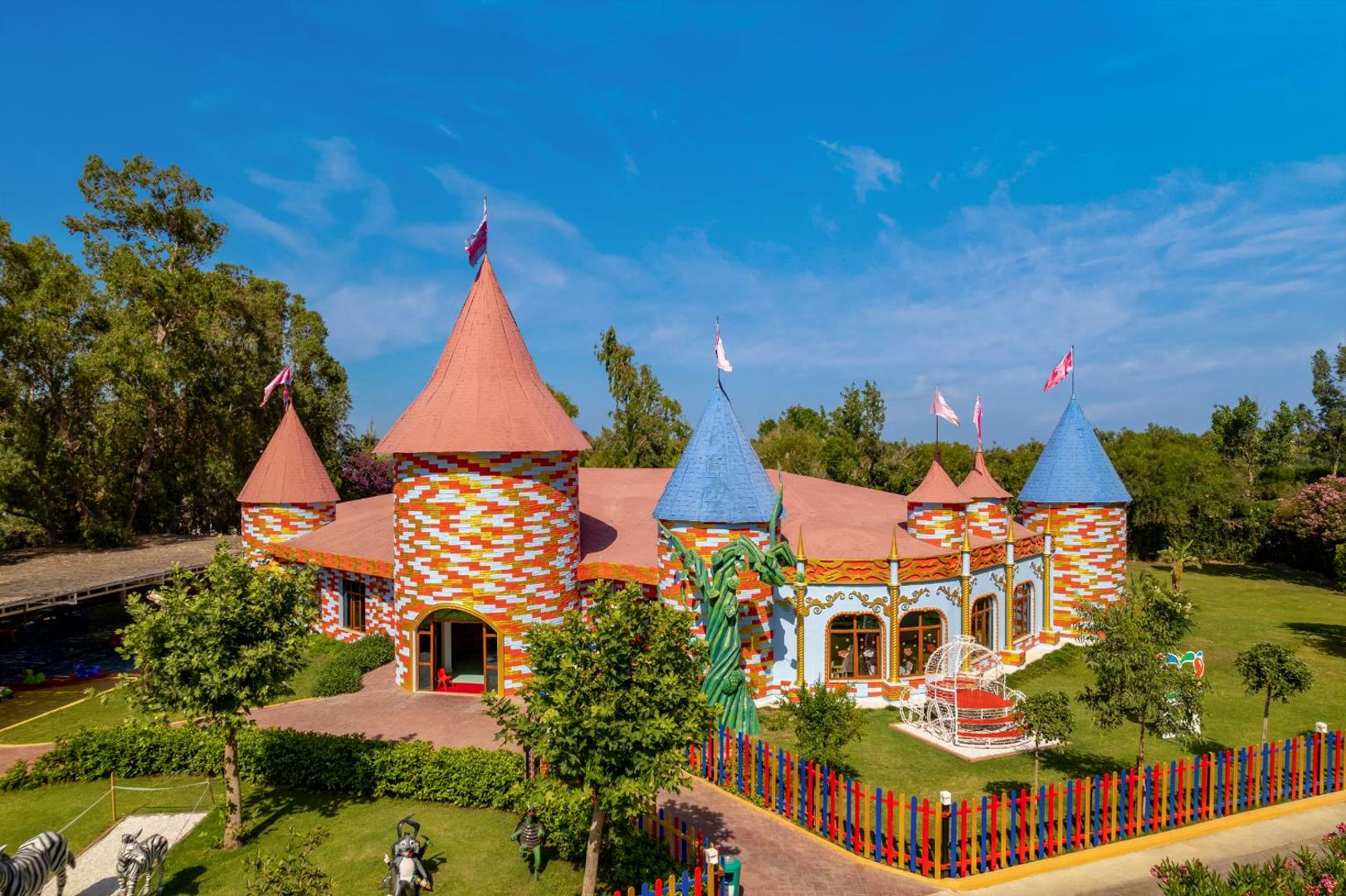 Delphin Be Grand Resort bērnu klubs krāsainas pils formā ar rotaļu laukumu un zaļu zālienu kūrorta teritorijā Antalijā