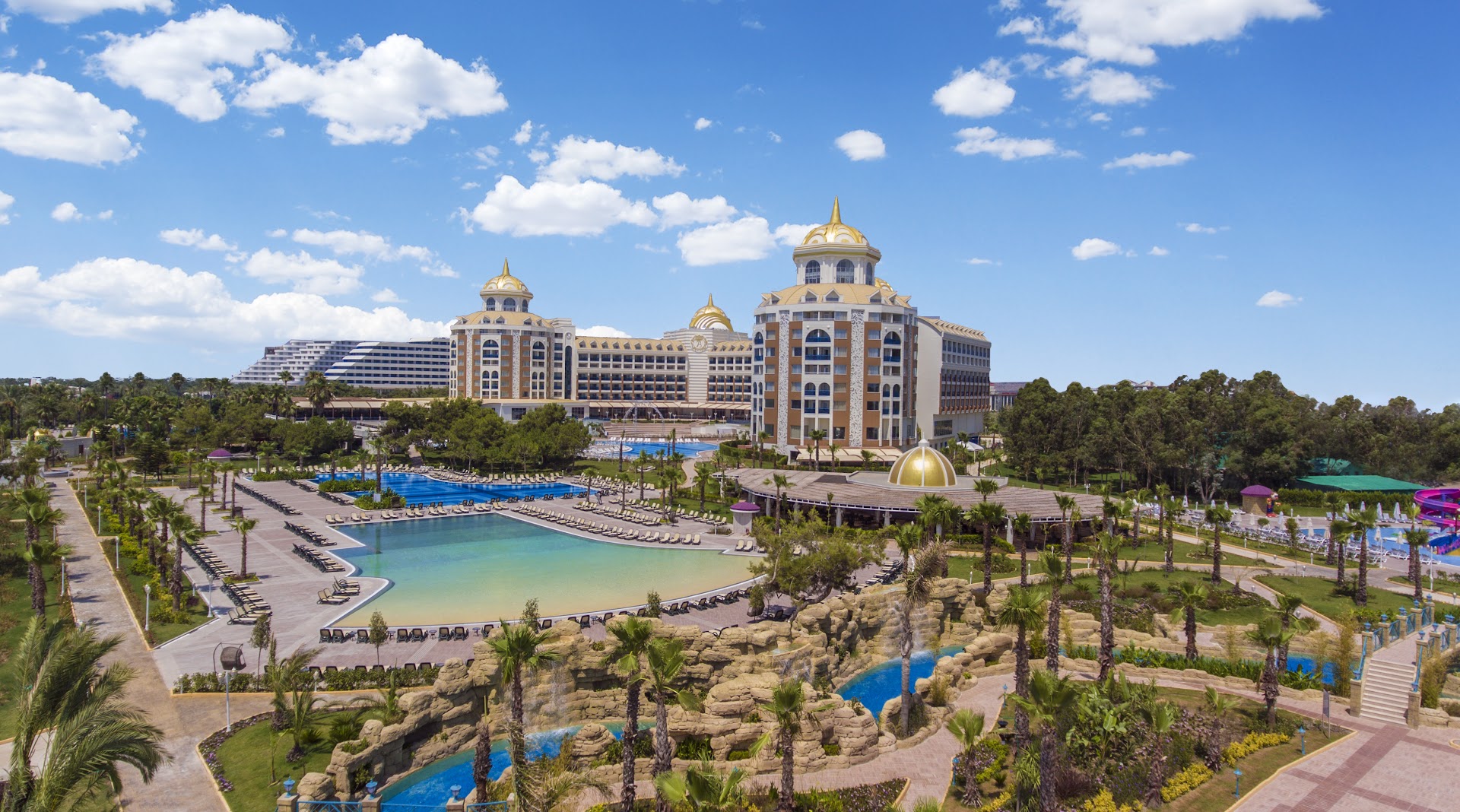 Delphin Be Grand Resort āra baseini ar mākslīgajām klintīm un ūdenskritumiem — plaša atpūtas zona un viesnīcas korpusi fonā