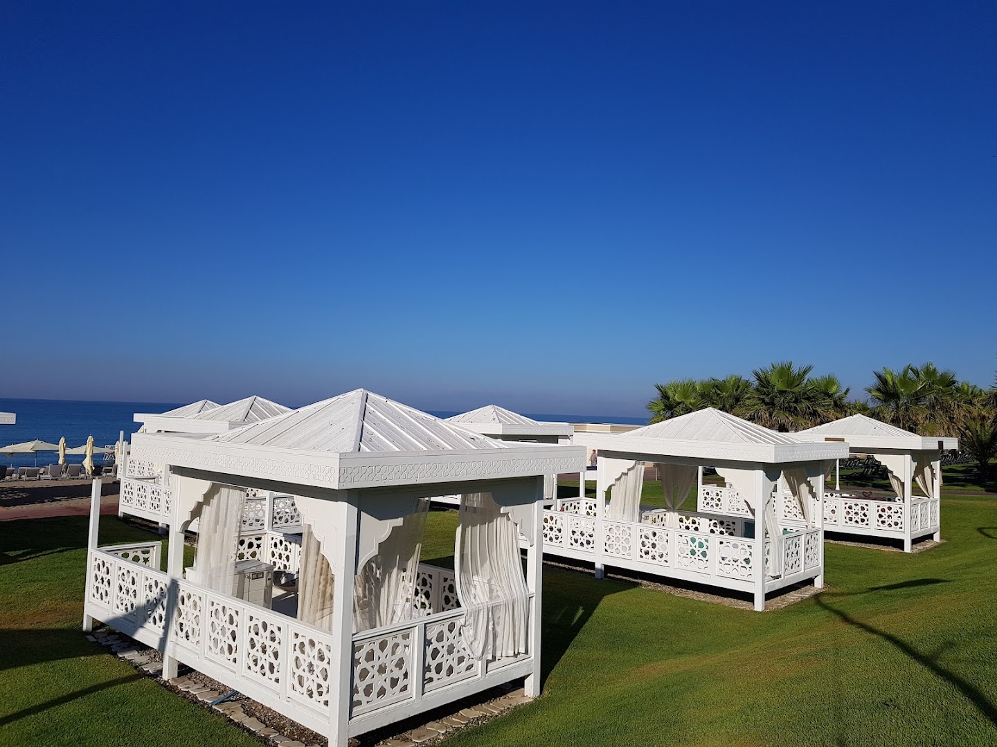 Gural Premier Belek dārza zonā izvietotas baltas atpūtas lapenes uz zaļa zālāja — grezna vide atpūtai kūrorta teritorijā