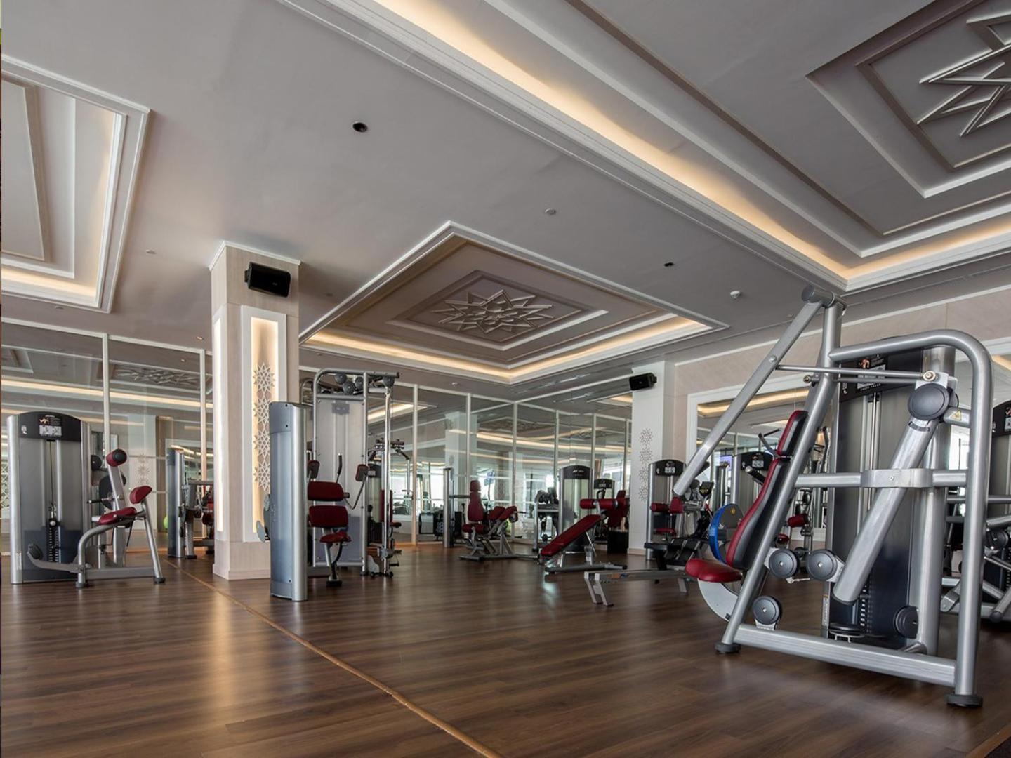 Gural Premier Belek plaša fitness zāle ar moderniem spēka trenažieriem, spoguļu sienām un koka grīdas segumu