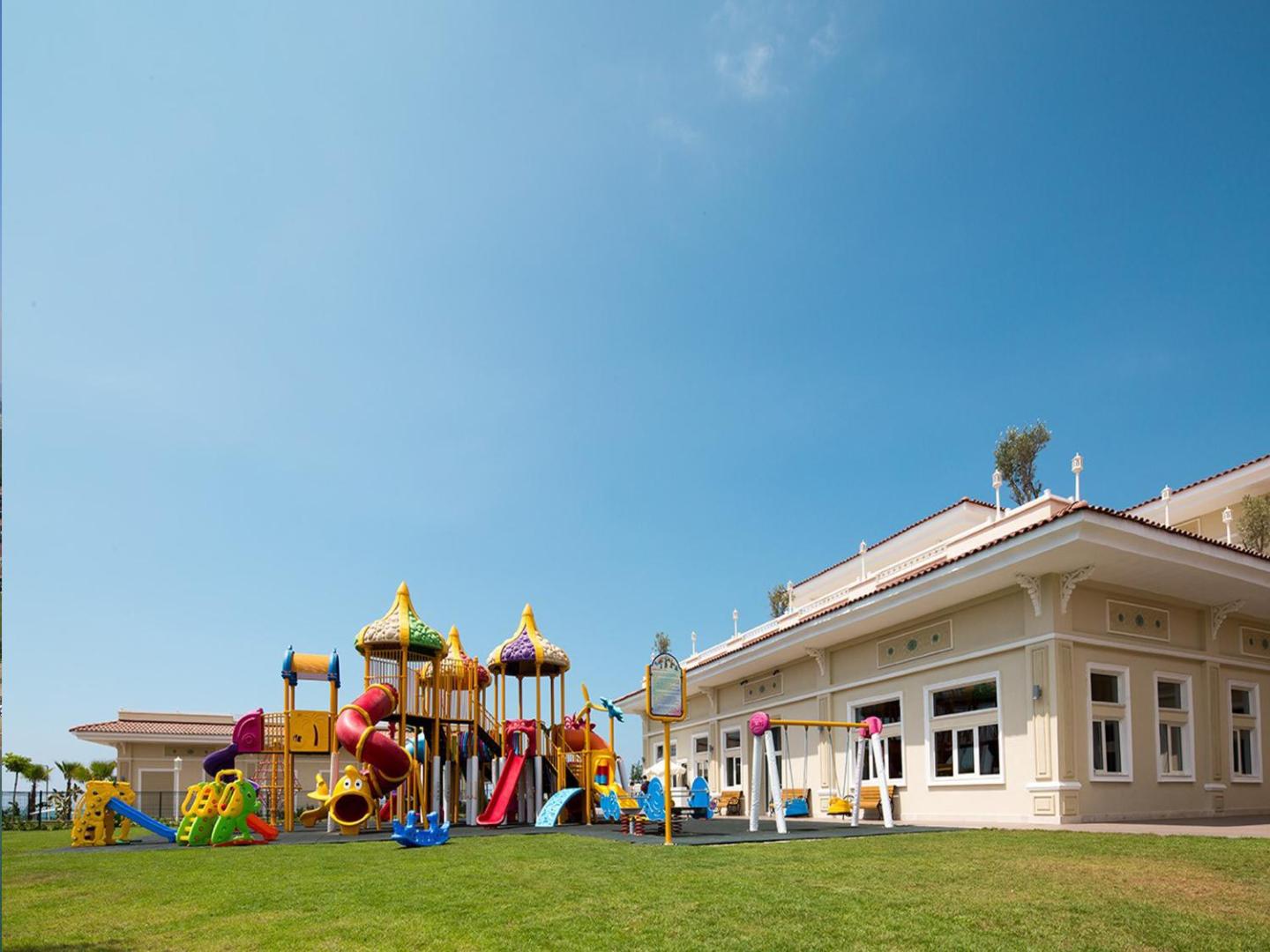 Gural Premier Belek bērnu rotaļu laukums ar krāsainiem slidkalniņiem un šūpolēm uz mīksta seguma pie kūrorta ēkas Belekā, Turcijā