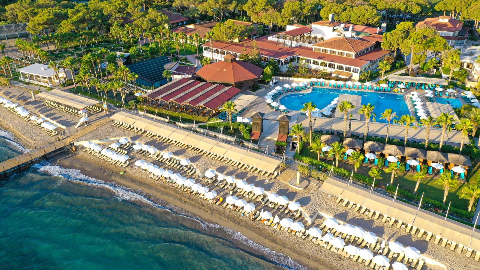 Crystal Flora Beach Resort aerofoto skats uz plašo teritoriju, baseiniem un privāto pludmali Beldibi reģionā, Turcijā, saulrieta gaismā.