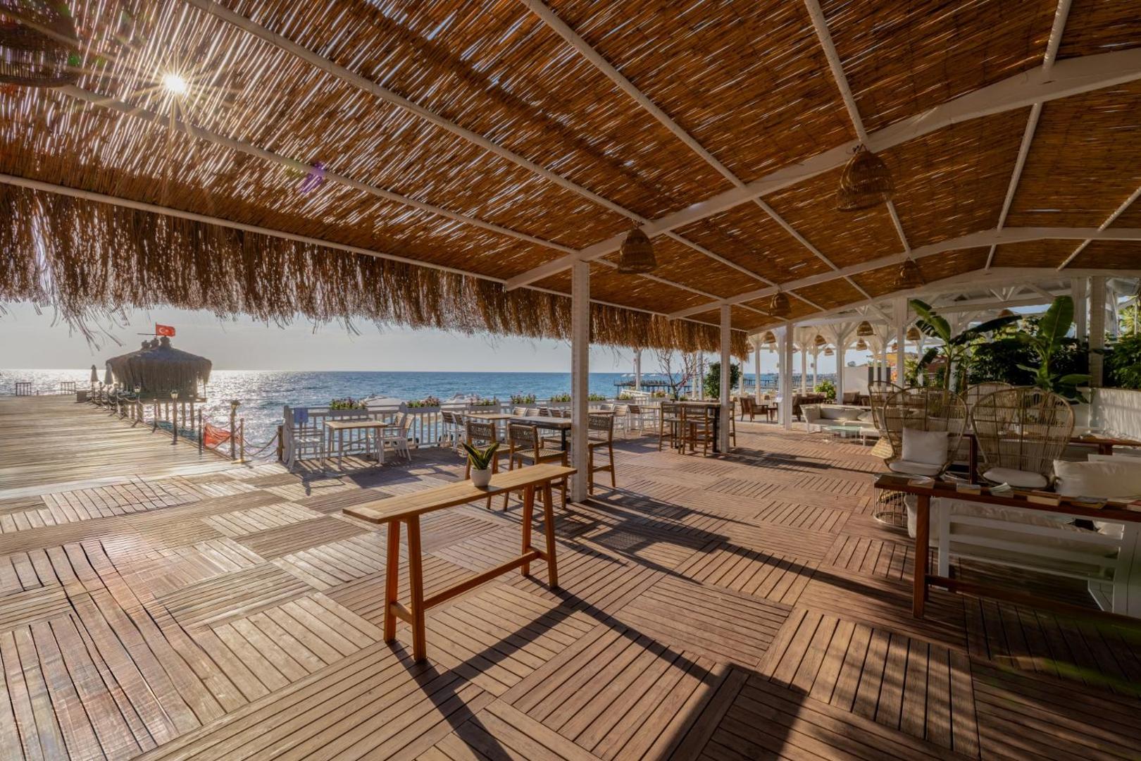 Crystal Flora Beach Resort atpūtas zona pie jūras zem salmu nojumes ar koka mēbelēm un skatu uz Vidusjūru