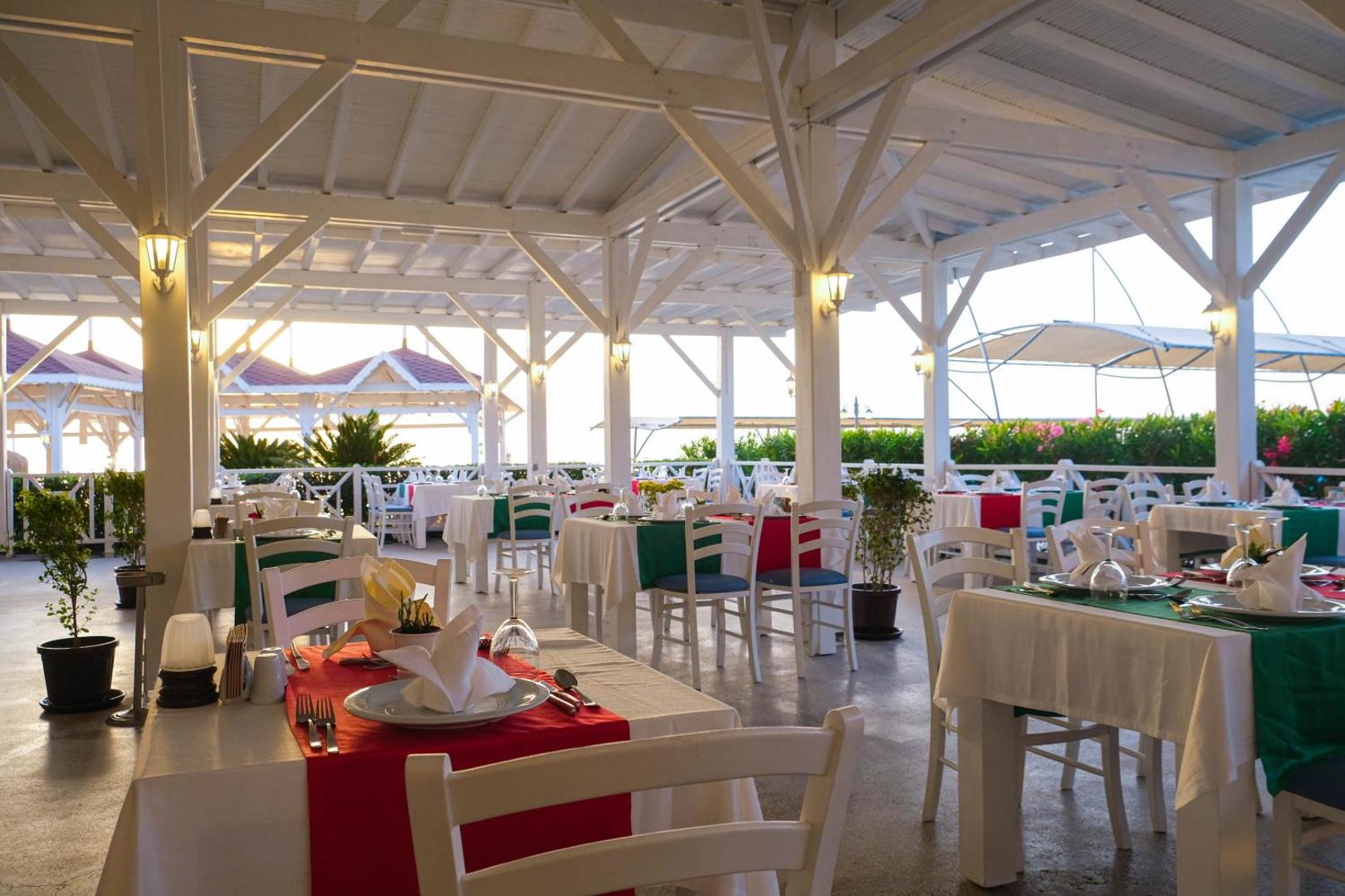 Crystal Flora Beach Resort restorāns ar baltām koka konstrukcijām un krāsainiem galda klājumiem atvērtā tipa terasē