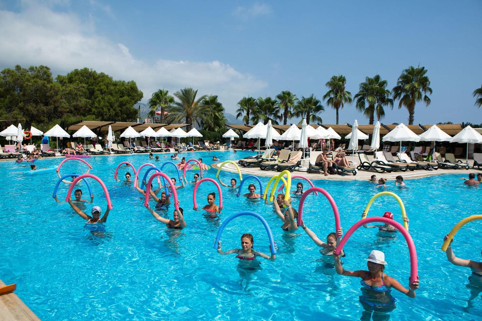 Viesi piedalās ūdens aerobikas nodarbībā Crystal Flora Beach Resort baseinā — aktīva izklaide un animācijas programma saulainā dienā