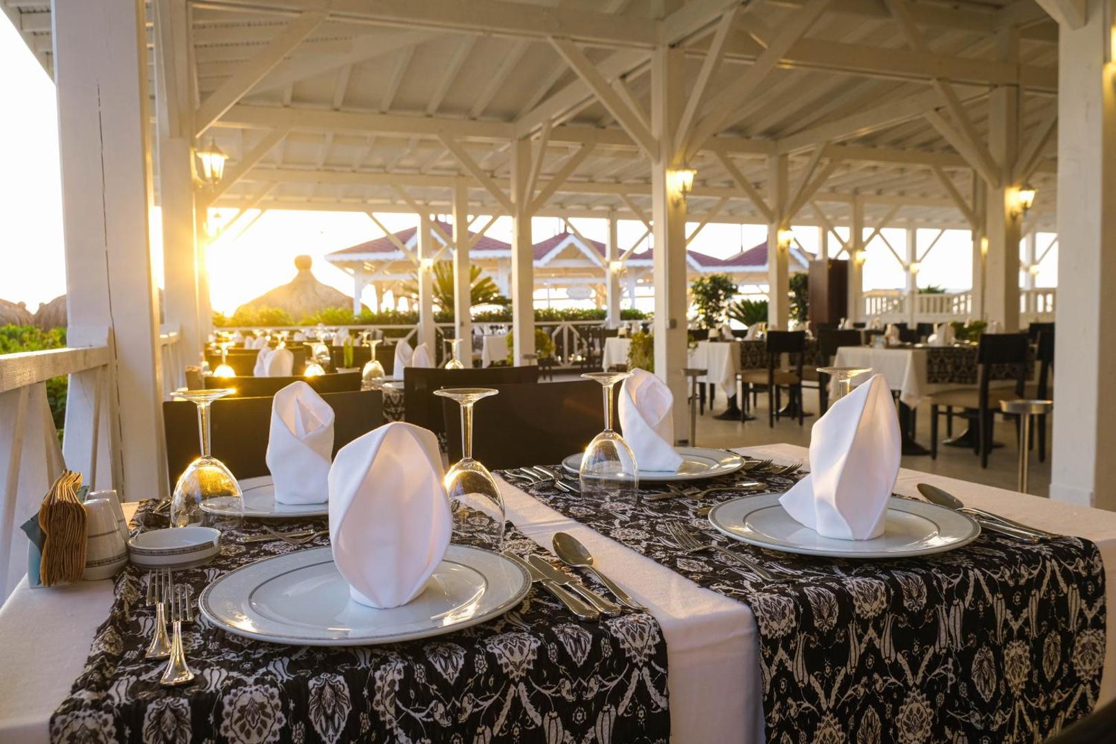 Crystal Flora Beach Resort restorāna terase ar klātiem galdiem saulrieta laikā — elegants galda klājums ar baltām salvetēm
