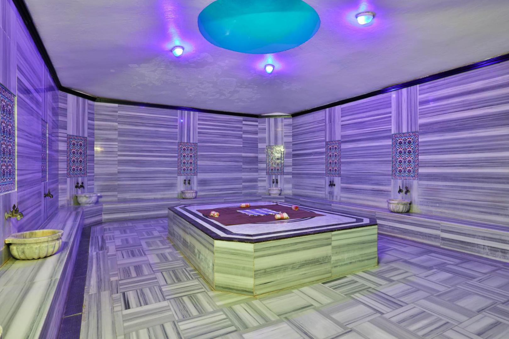 Tradicionāls turku hamams Crystal Flora Beach Resort spa centrā ar marmora apdari, centrālo akmens platformu un dekoratīvu apgaismojumu.