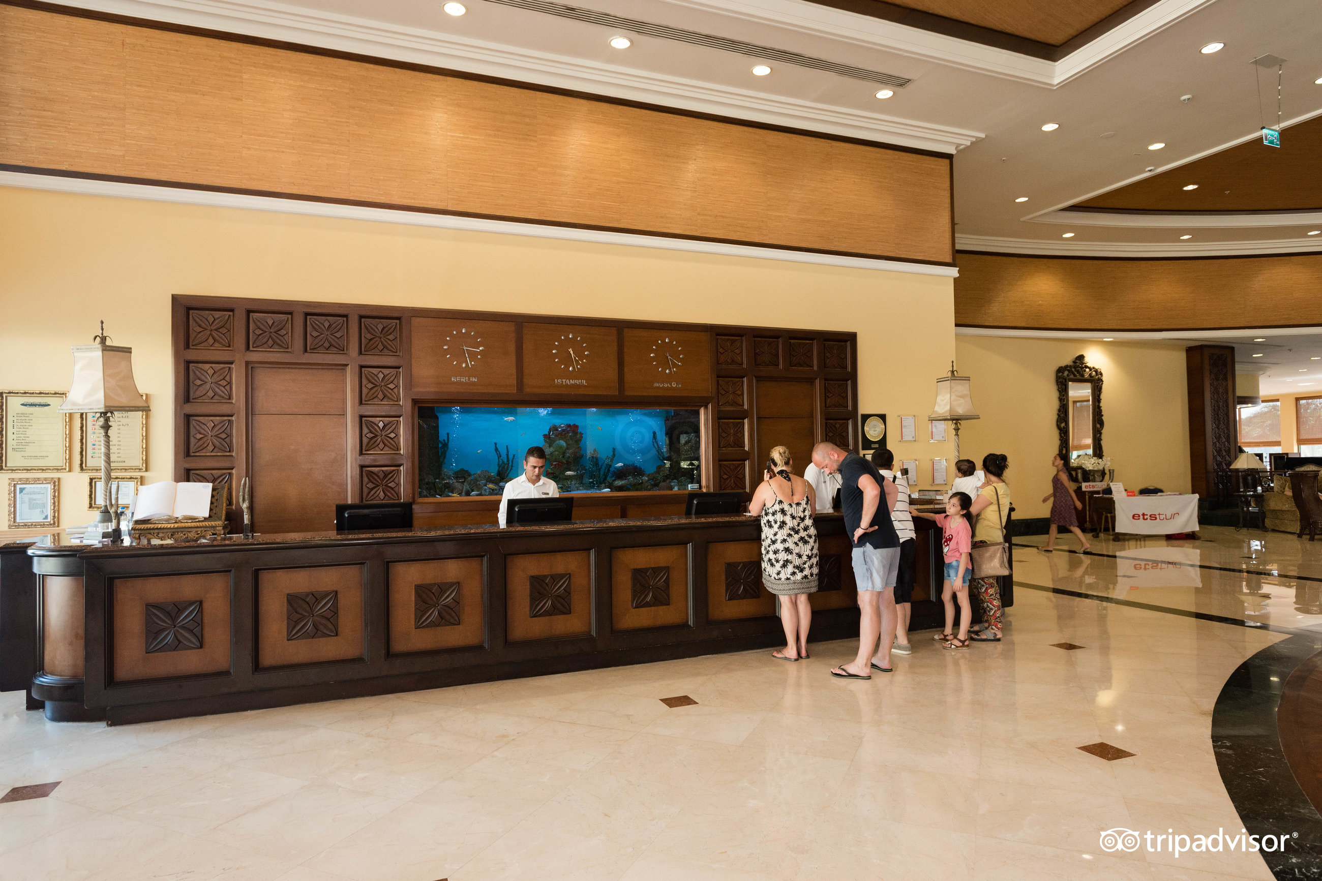 Viesnīcas IC Hotels Green Palace recepcijas zona ar koka apdari, akvāriju un viesmīlīgu personālu Antalijas kūrortā