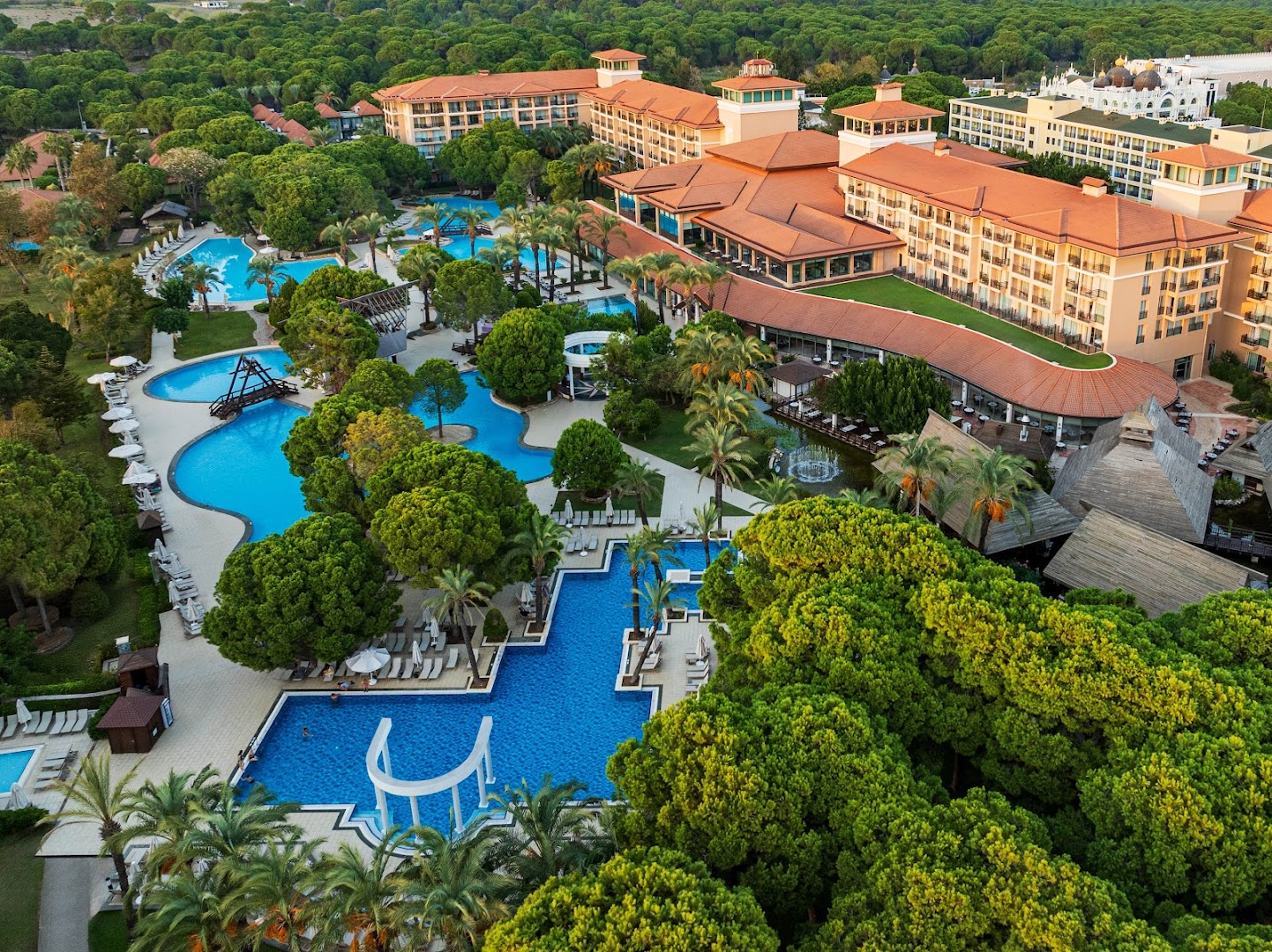 IC Hotels Green Palace viesnīcas teritorija no augšas Antalijā — plaši zili baseini, sulīgi zaļi dārzi un kūrorta ēkas saulrietā