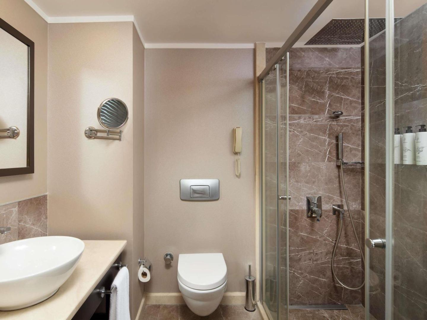 TUI Magic Life Rixos Beldibi viesnīcas numura vannas istaba ar modernu dušas kabīni, marmora flīzēm un baltu santehniku Beldibi reģionā, Turcijā.