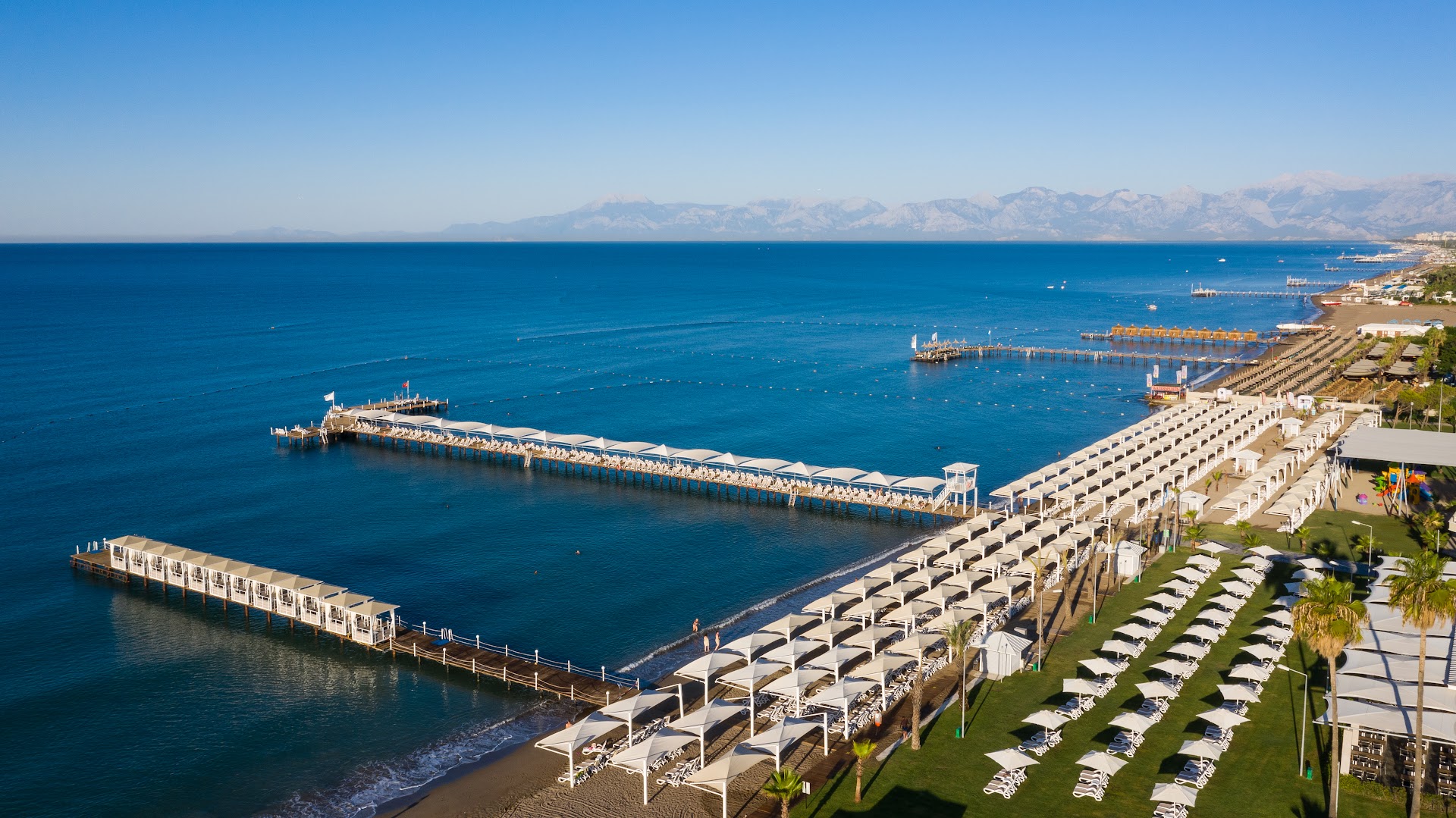 Swandor Hotels & Resorts Topkapi Palace privātā pludmale ar garām koka piestātnēm un saulessargu rindām Vidusjūras piekrastē