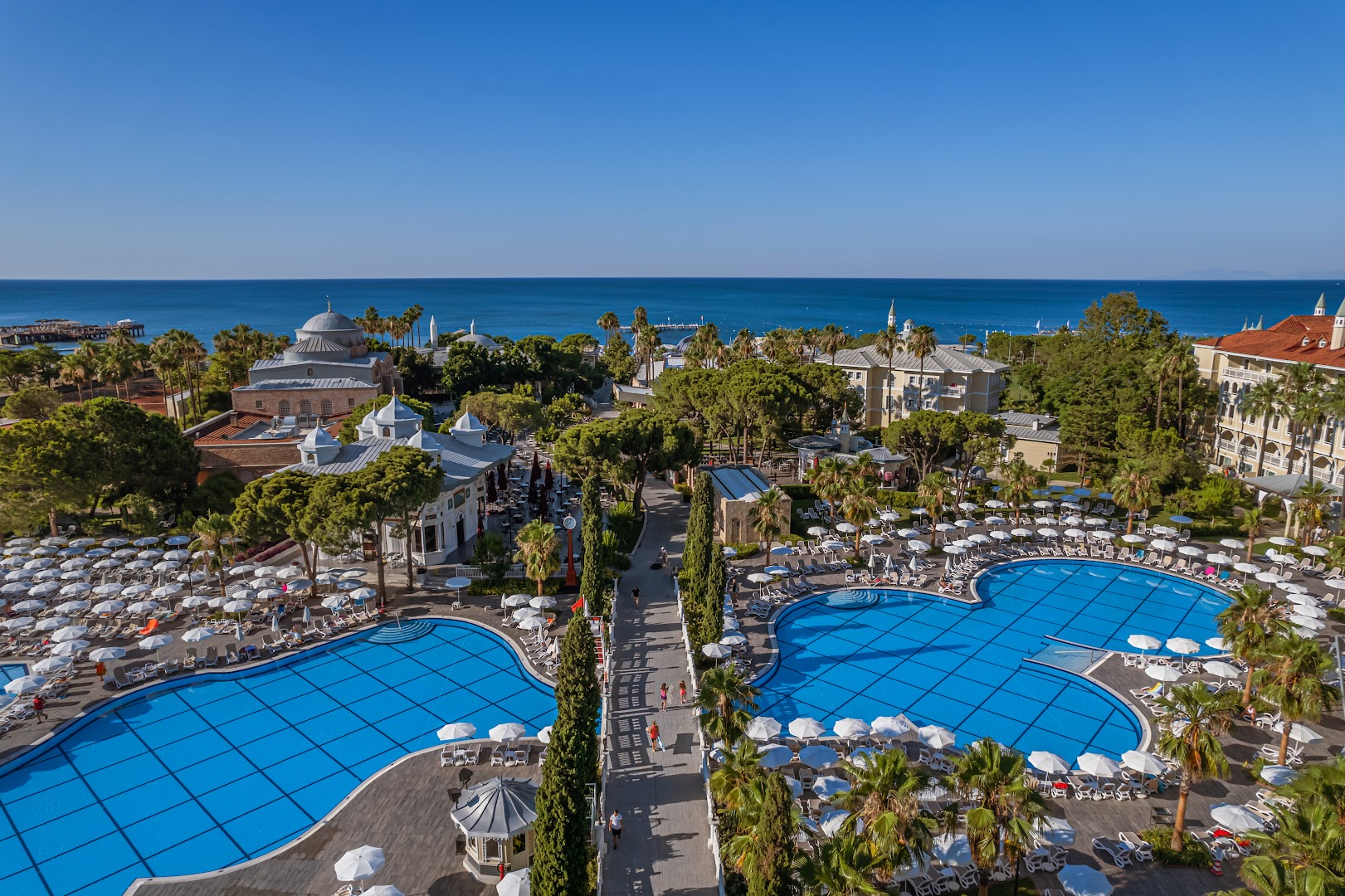 Panorāmas skats uz Swandor Hotels & Resorts Topkapi Palace teritoriju ar lieliem baseiniem, palmām un Vidusjūru fonā Antalijas piekrastē