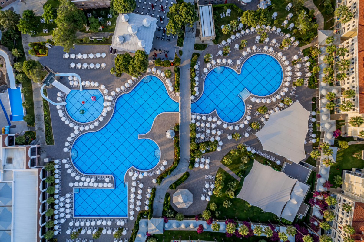 Aerofoto skats no augšas uz Swandor Hotels & Resorts Topkapi Palace baseinu kompleksu, saulessargiem un atpūtas zonām dārza ieskāvumā