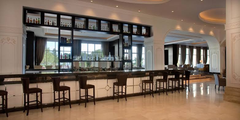 Juju Premier Palace viesnīcas lobby bārs ar modernu apgaismojumu un tumša koka leti — plaša atpūtas zona ar bāra krēsliem