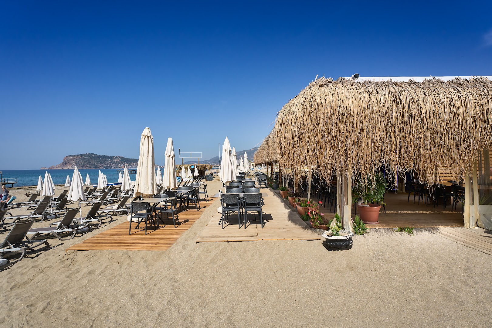 Kaila Beach Hotel pludmales bārs ar salmu jumtu un galdiņiem uz smiltīm Alanjā, Turcijā — skats uz jūru