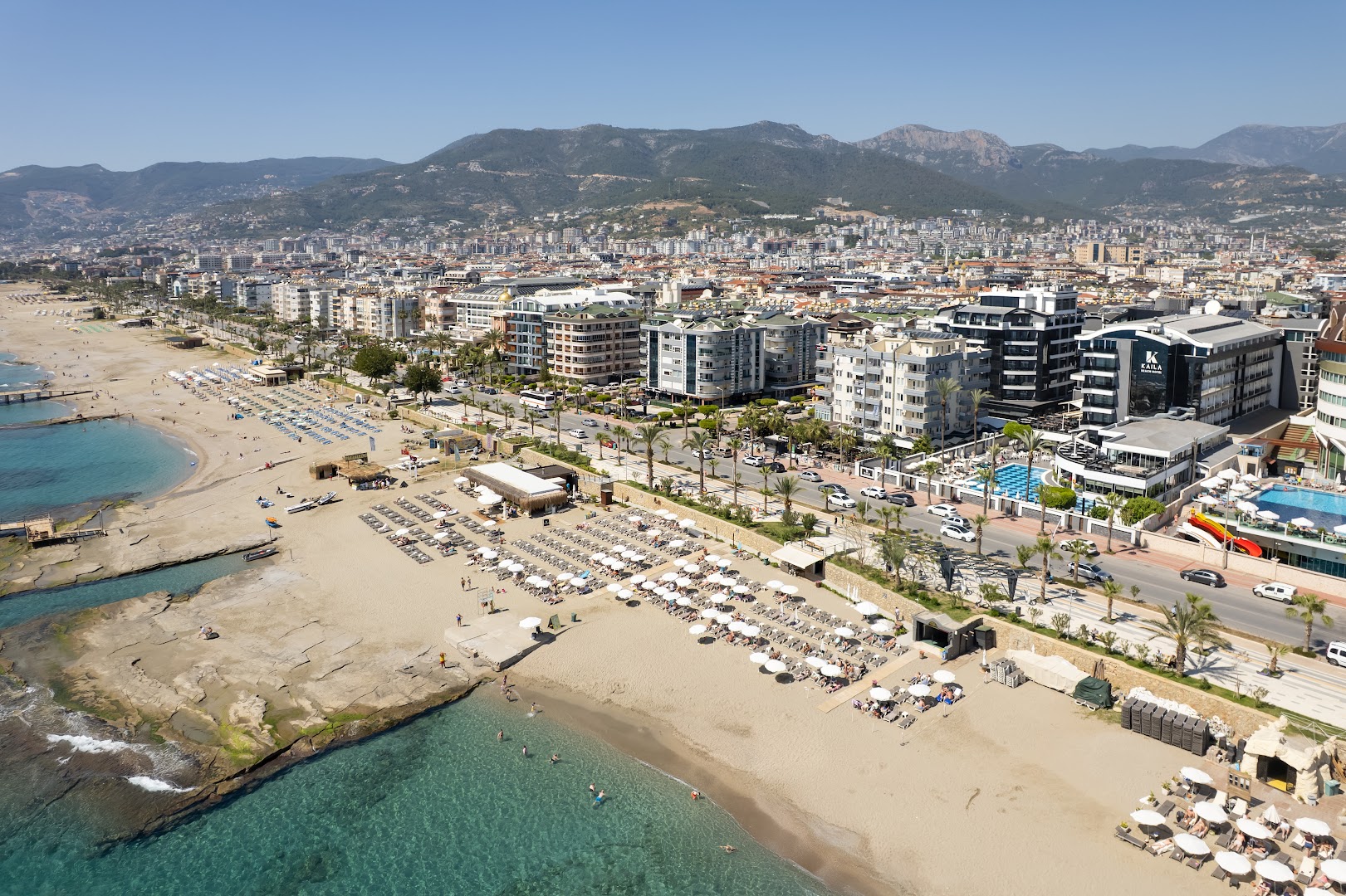 Aerofoto skats uz Kaila Beach Hotel Alanjā, parādot viesnīcas atrašanās vietu piekrastē, pilsētas panorāmu un kalnus fonā