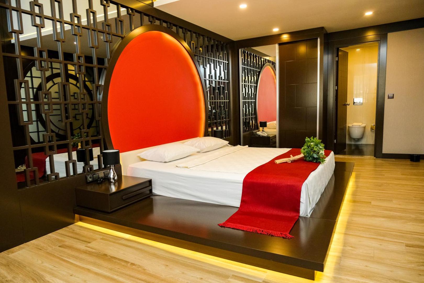 Kaila Beach Hotel luksusa numurs ar īpašu dizainu, sarkanu dekoratīvu elementu pie gultas un koka grīdu