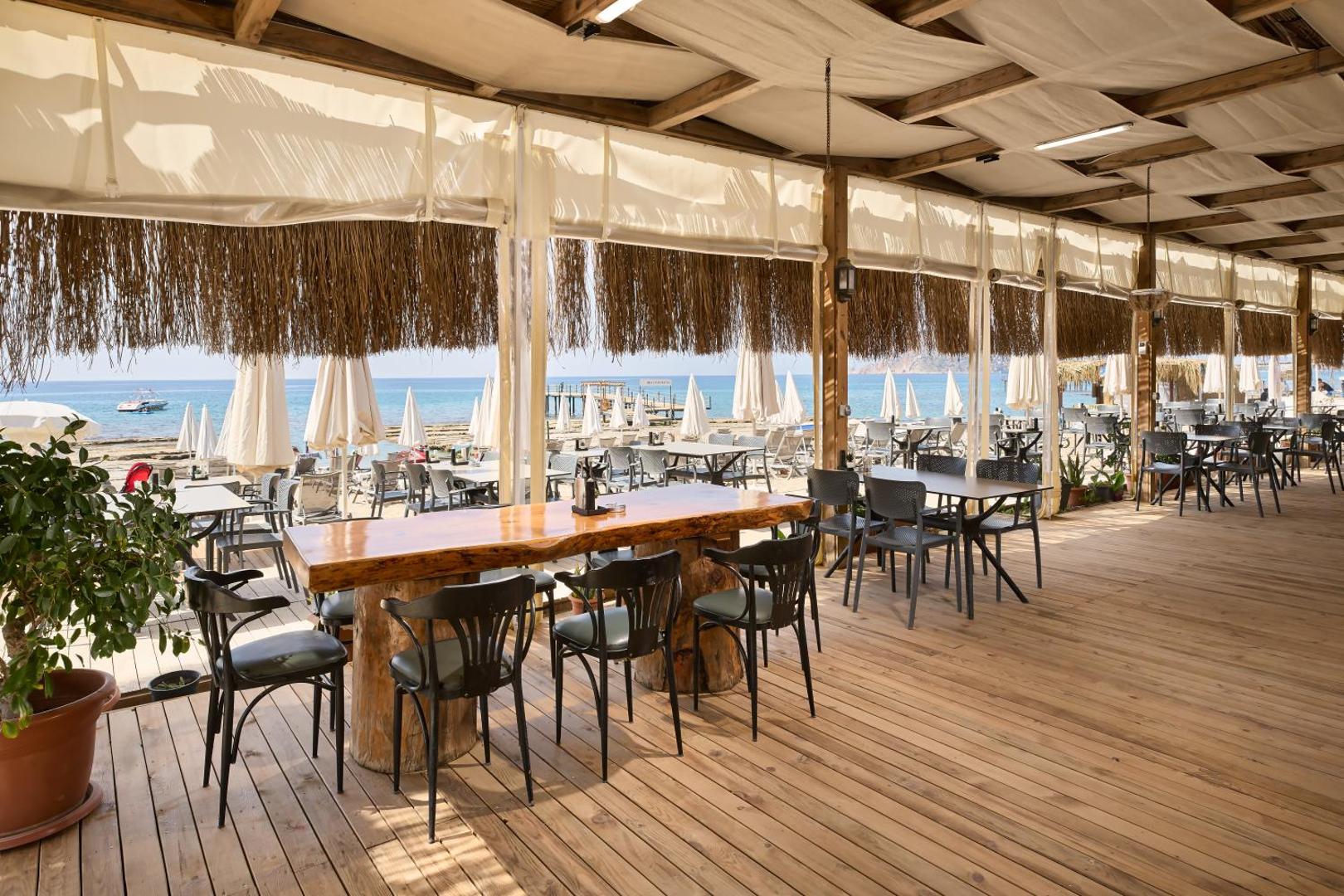 Kaila Beach Hotel pludmales bārs un restorāns Alanjā ar koka terasi, masīvkoka galdiem un skatu uz Vidusjūru