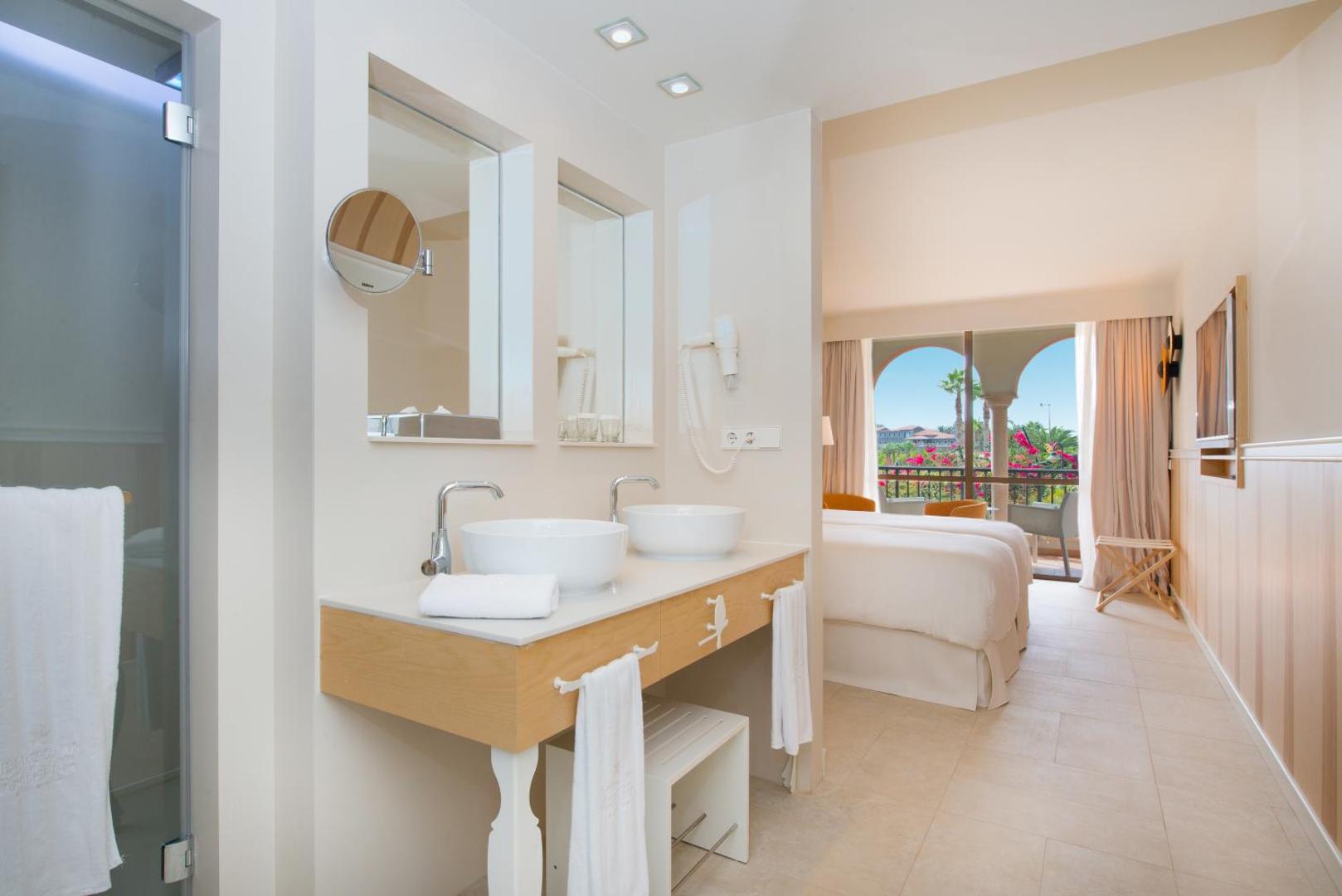 Iberostar Selection Anthelia moderns numurs ar gaišu vannasistabu, dubulto izlietni un skatu uz dārzu caur balkona durvīm