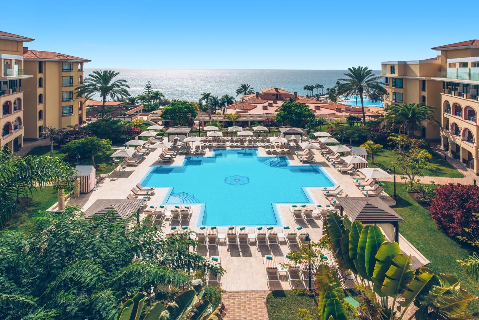 Iberostar Selection Anthelia viesnīcas iekšpagalms ar centrālo baseinu, dārzu un numuru korpusiem Tenerifē — skats uz okeānu tālumā