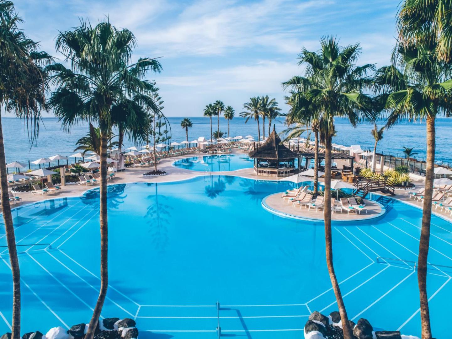 Iberostar Selection Anthelia galvenais baseins ar bāru un atpūtas zonu starp palmām pie okeāna Tenerifē.