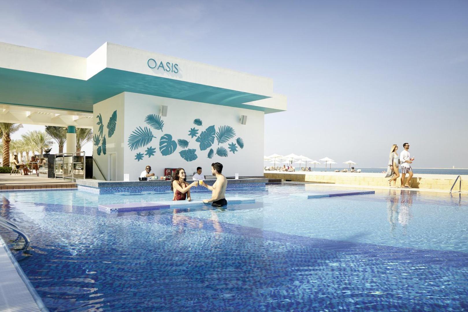 RIU Dubai viesnīcas Oasis baseina bārs, kur viesi ūdenī malko dzērienus saulainā dienā pie Persijas līča krasta.