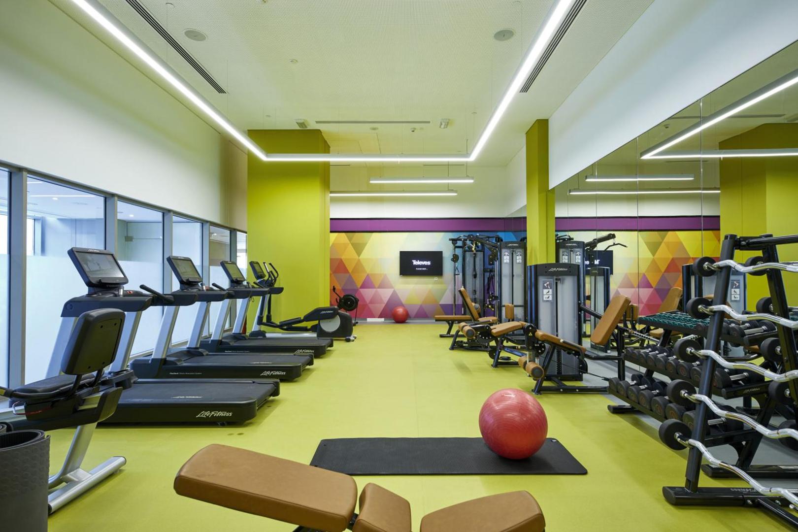 Mūsdienīgs RIU Dubai fitness centrs ar skrejceliņiem, svariem un vingrošanas bumbām gaišā, plašā telpā