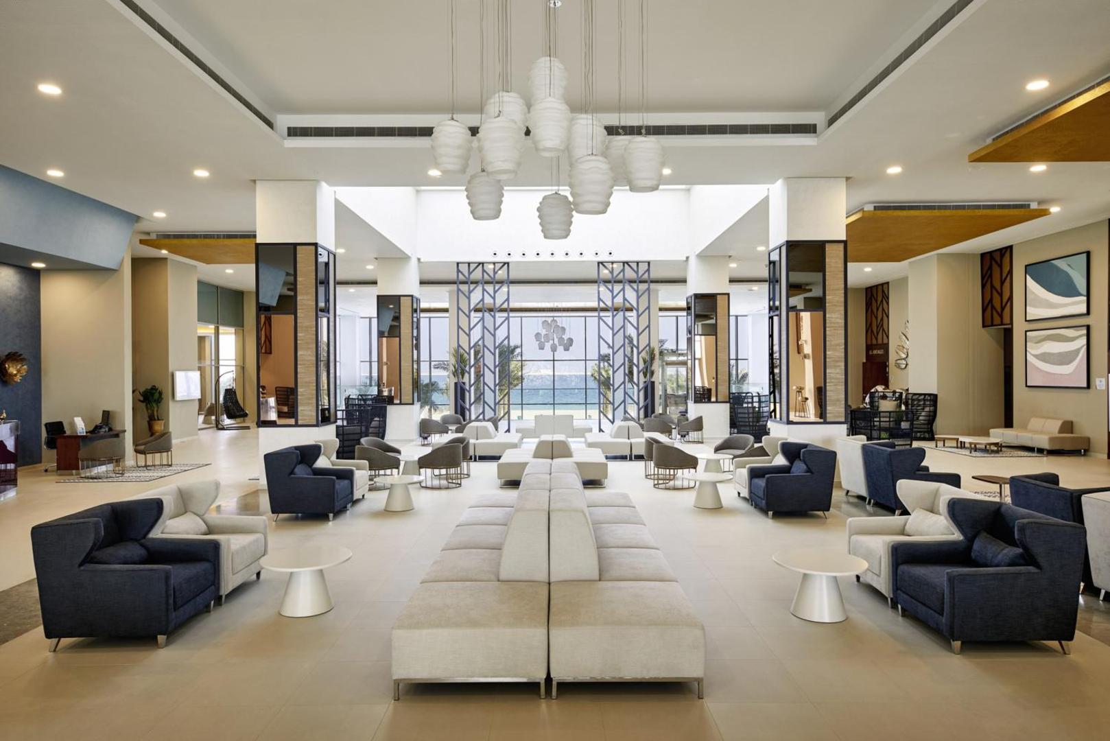 Viesnīcas RIU Dubai plašais un modernais lobby ar gaišiem dīvāniem, augstiem griestiem un skatu uz jūru