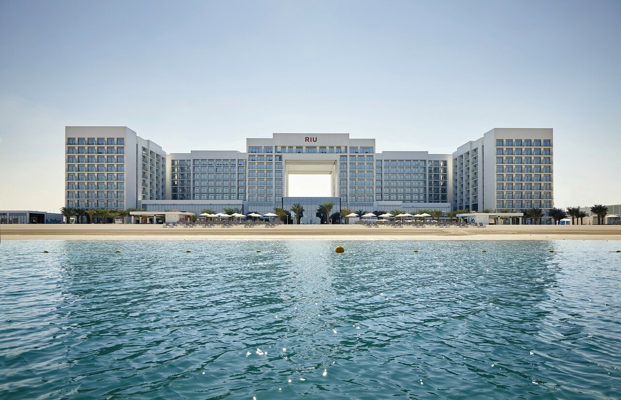Viesnīcas RIU Dubai modernā ēka pie Persijas līča krasta līnijas — skats no ūdens uz balto fasādi un smilšu pludmali