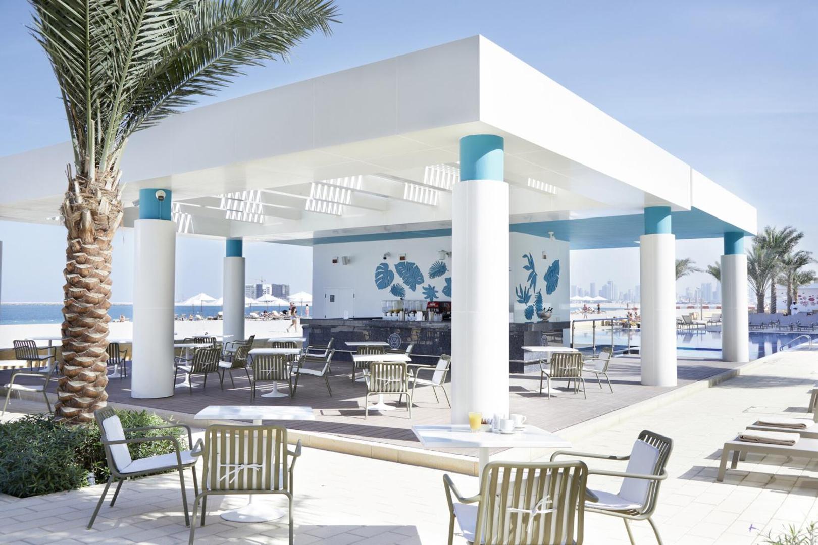 RIU Dubai pludmales bārs ar baltu nojumi, galdiņiem un skatu uz smilšu pludmali un zilo jūru