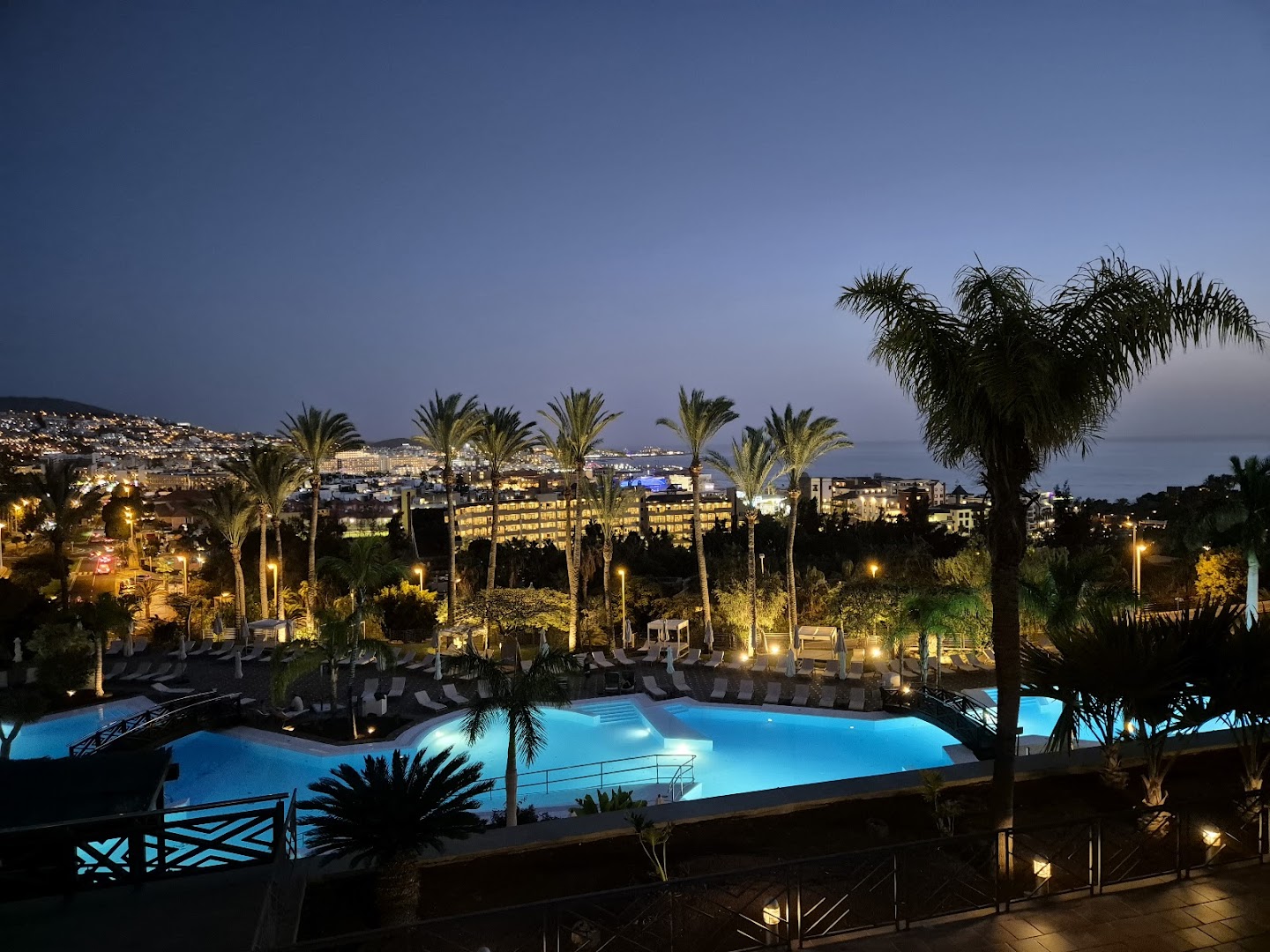 Meliá Jardines del Teide izgaismots āra baseins naktī ar palmām un pilsētas gaismām fonā Tenerifē