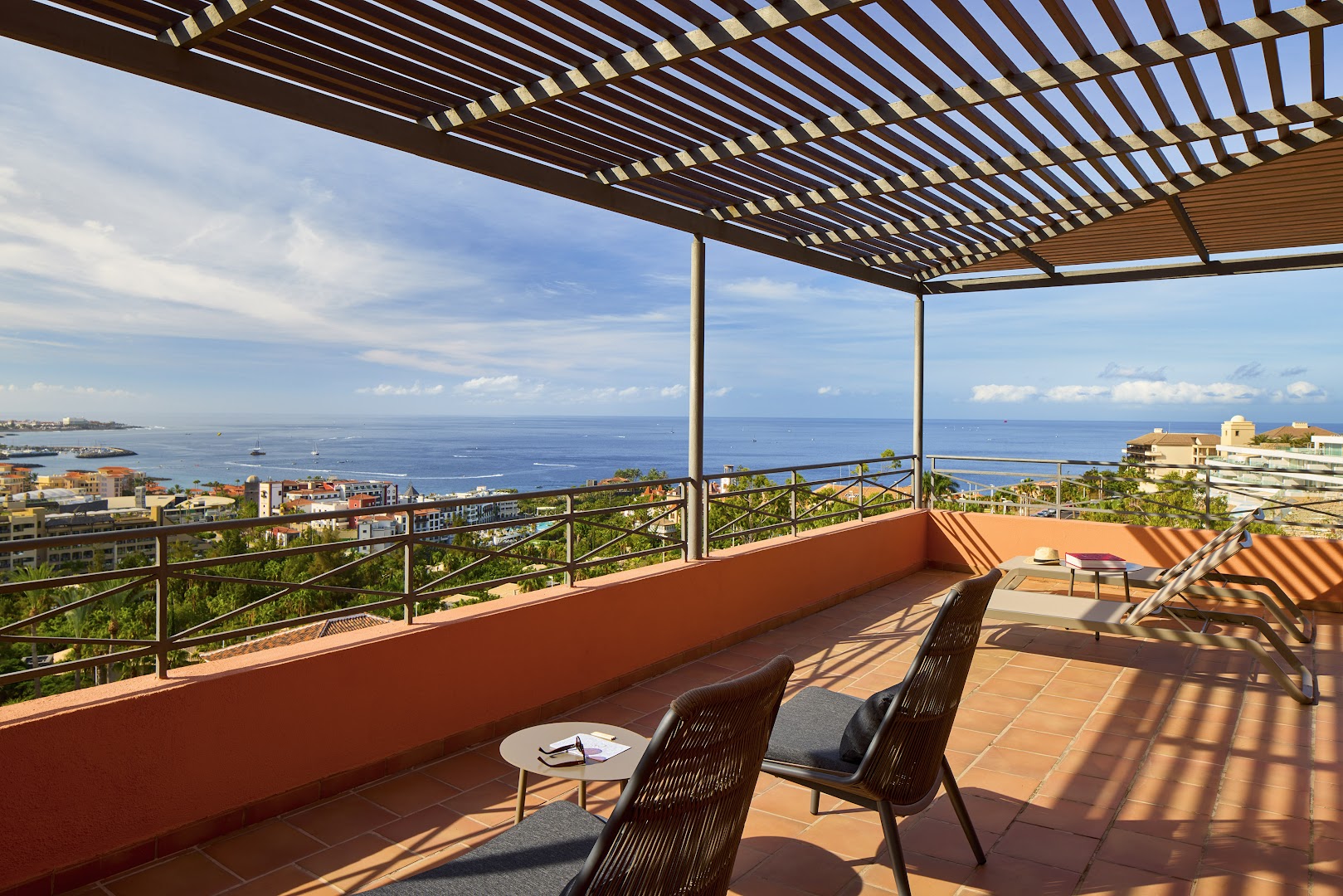Meliá Jardines del Teide plaša terase ar skatu uz okeānu Tenerifē — koka nojume, atpūtas krēsli un panorāmas skats uz piekrasti