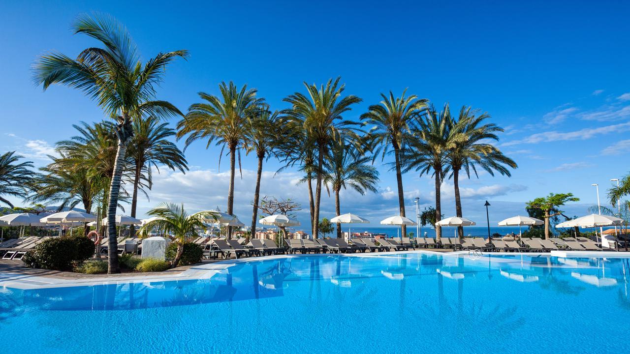 Tuvplāns Melia Jardines del Teide baseinam ar atspulgiem, rindu ar palmām un saulessargiem zem skaidrām debesīm