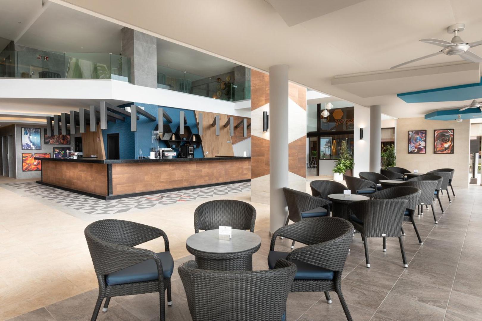 Riu Buena Vista plašā āra terase ar bāru, tumšiem pītiem krēsliem un modernu arhitektūru Tenerifes piekrastē