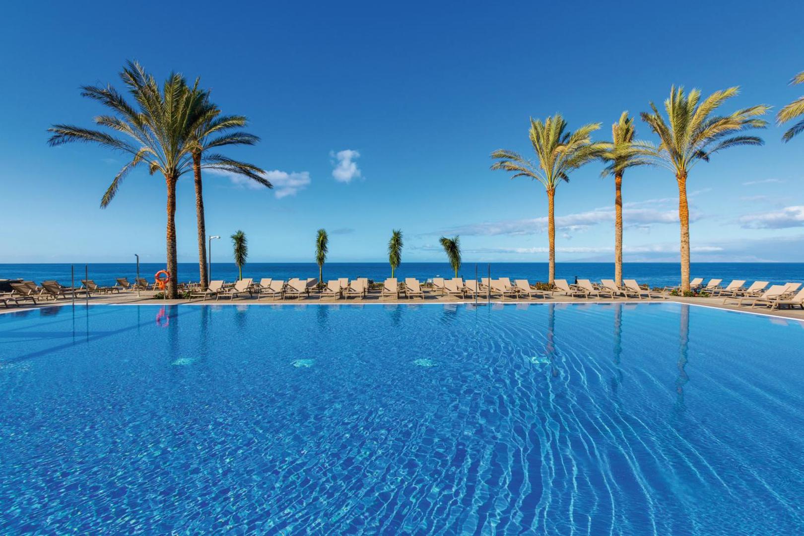 Riu Buena Vista bezgalības tipa baseins ar skatu uz okeānu un palmām zilās debesīs Tenerifē