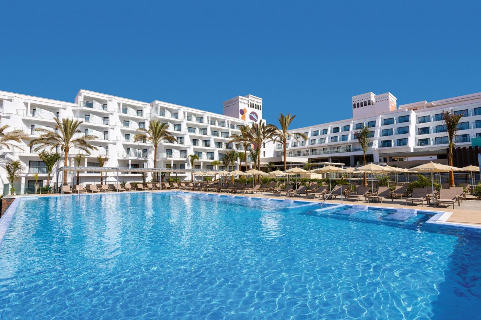 Riu Buena Vista viesnīcas ēka un lielais peldbaseins ar sauļošanās krēsliem un palmām Tenerifes piekrastē