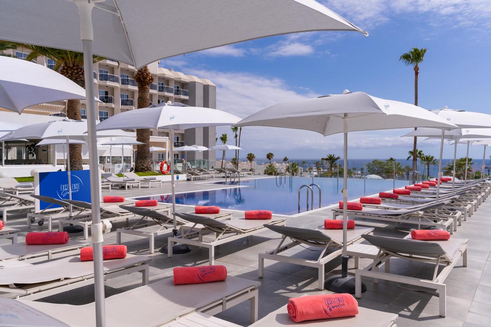 Hovima Cool Costa Adeje āra baseina zona ar sauļošanās krēsliem, saulessargiem un skatu uz okeānu Tenerifē