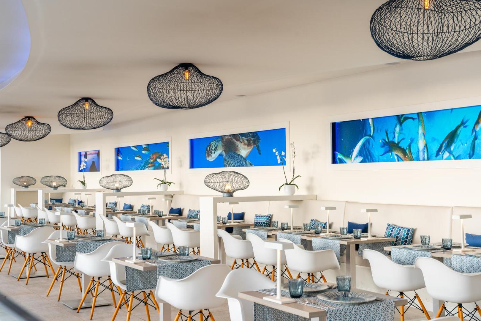 Hovima Cool Costa Adeje moderns restorāns ar baltiem krēsliem un okeāna tematikas gleznām pie sienām Tenerifē