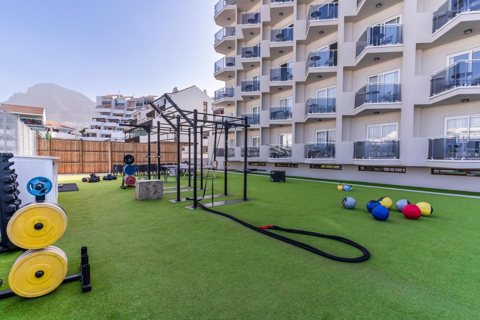 Hovima Cool Costa Adeje āra krosfita un fitnesa zona uz mākslīgā zālāja pie viesnīcas korpusa ar skatu uz kalniem.