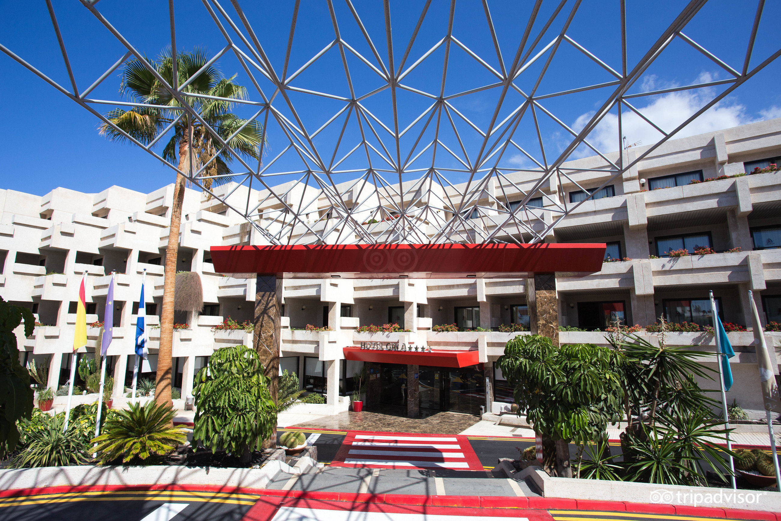 Alexandre Hotel Gala galvenā ieeja Playa de las Americas kūrortā Tenerifē ar modernu metāla konstrukcijas jumtu un palmām