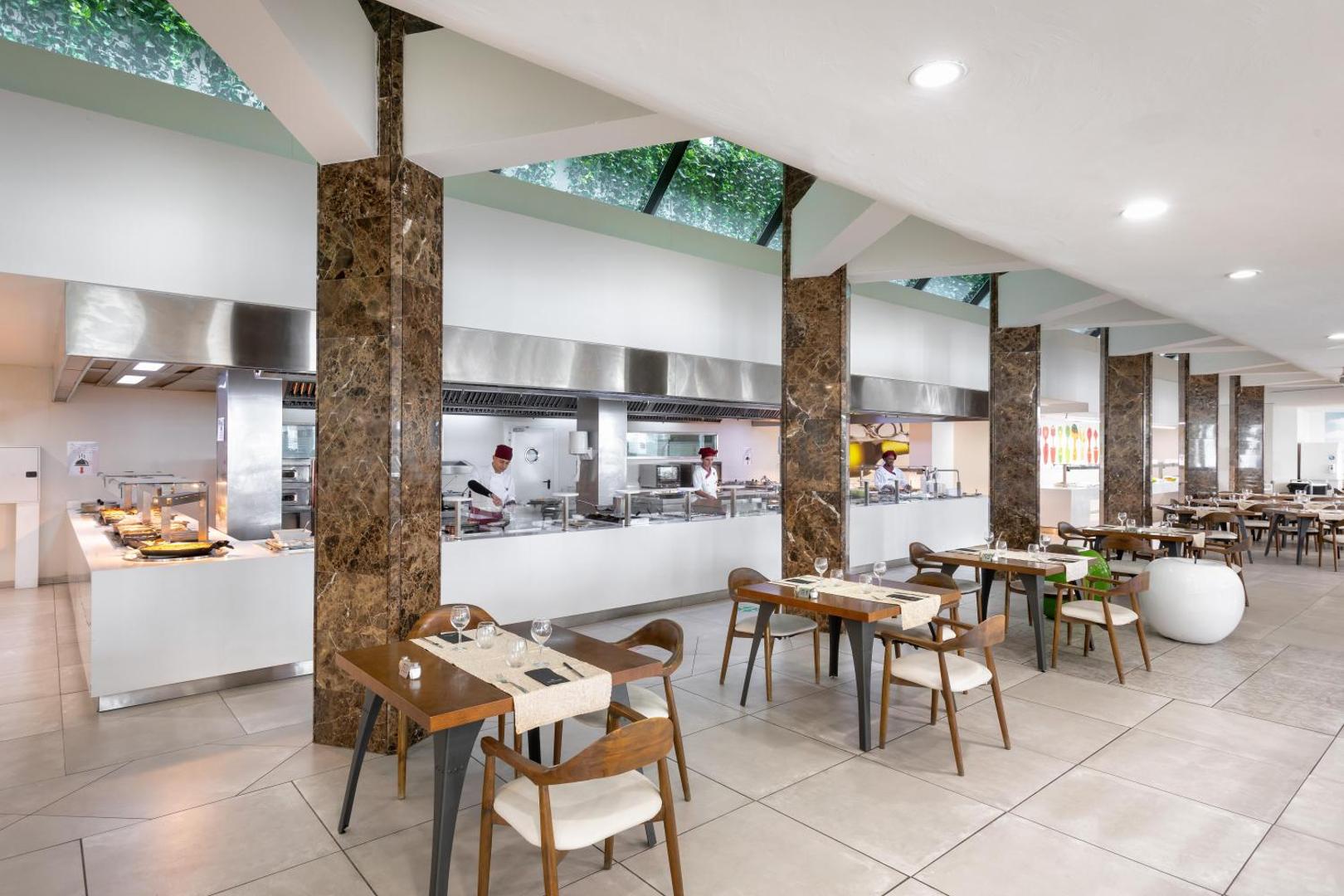 Alexandre Hotel Gala restorāna atvērtā tipa virtuve un bufetes zona — pavāri gatavo maltītes viesu klātbūtnē modernā vidē